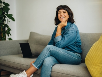 Smiling woman in denim jacket sitting on a couch