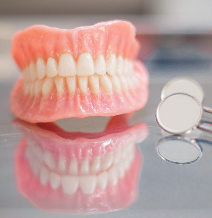 Full dentures resting on table next to dental mirrors