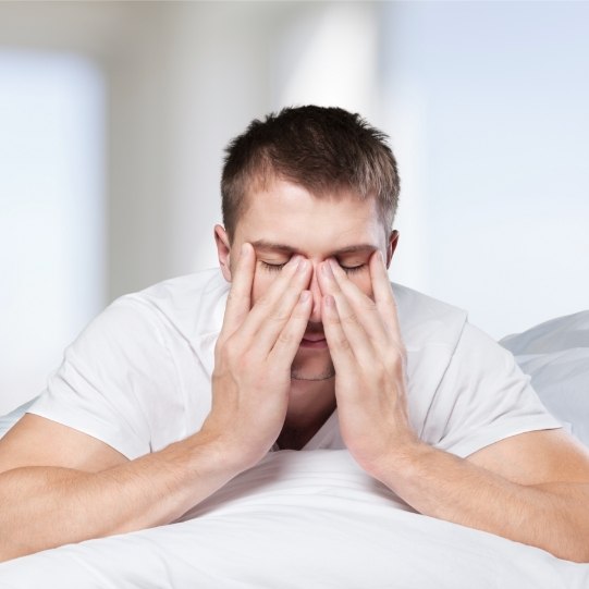 Man in bed rubbing his eyes before sleep apnea treatment in Mansfield