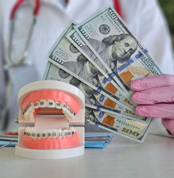 Person holding money next to dental braces model