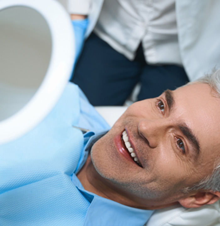 Man in dental chair smiling and looking at mirror