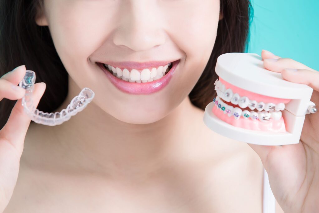 Nose-to-shoulder view of woman holding Invisalign in one hand and sample braces in the other