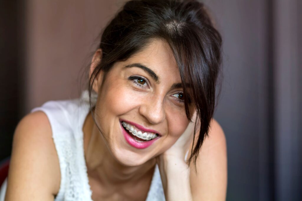 Woman in white tank top with braces on teeth smiling